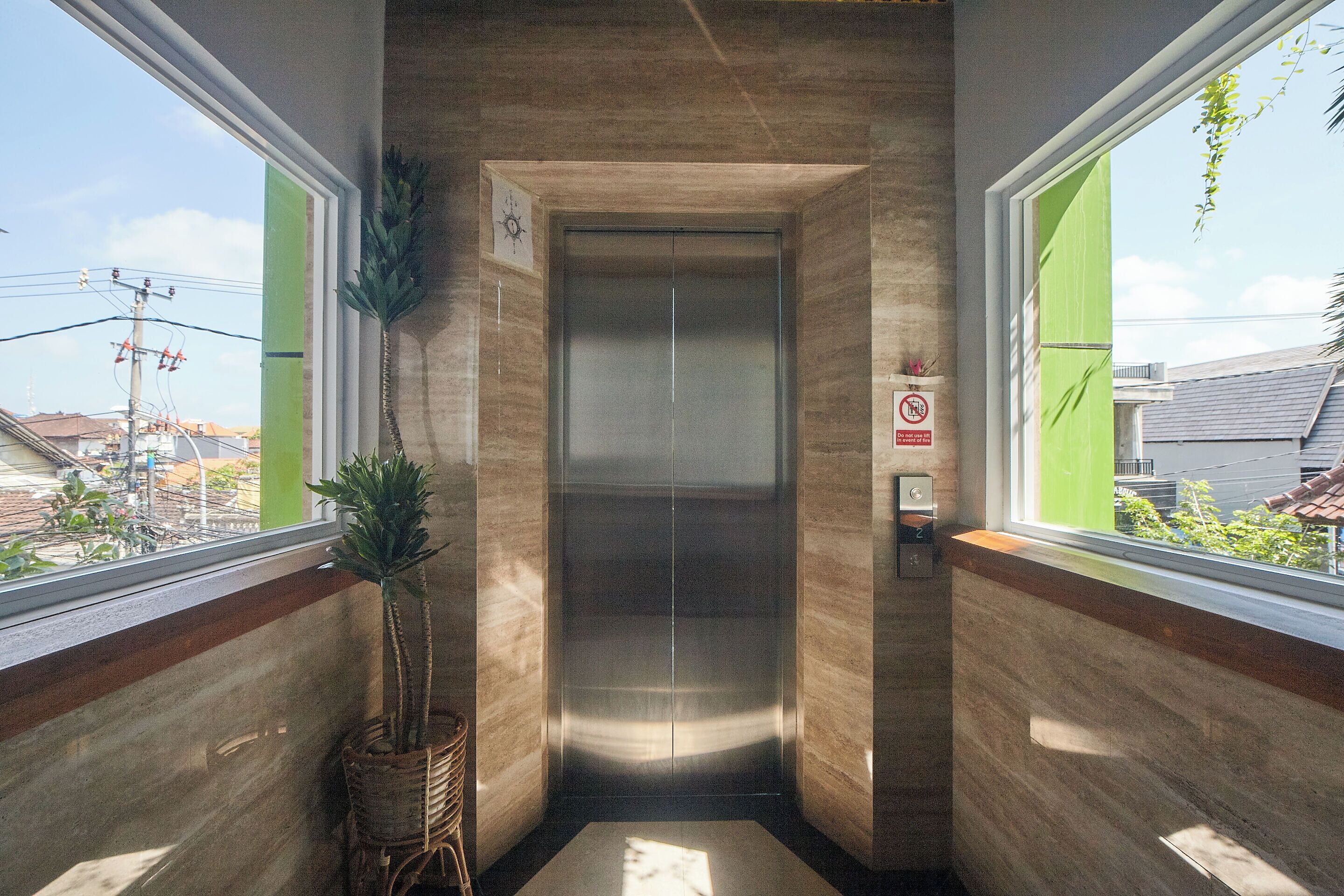 An elevator in a modern building with a wooden finish and a potted plant beside it.