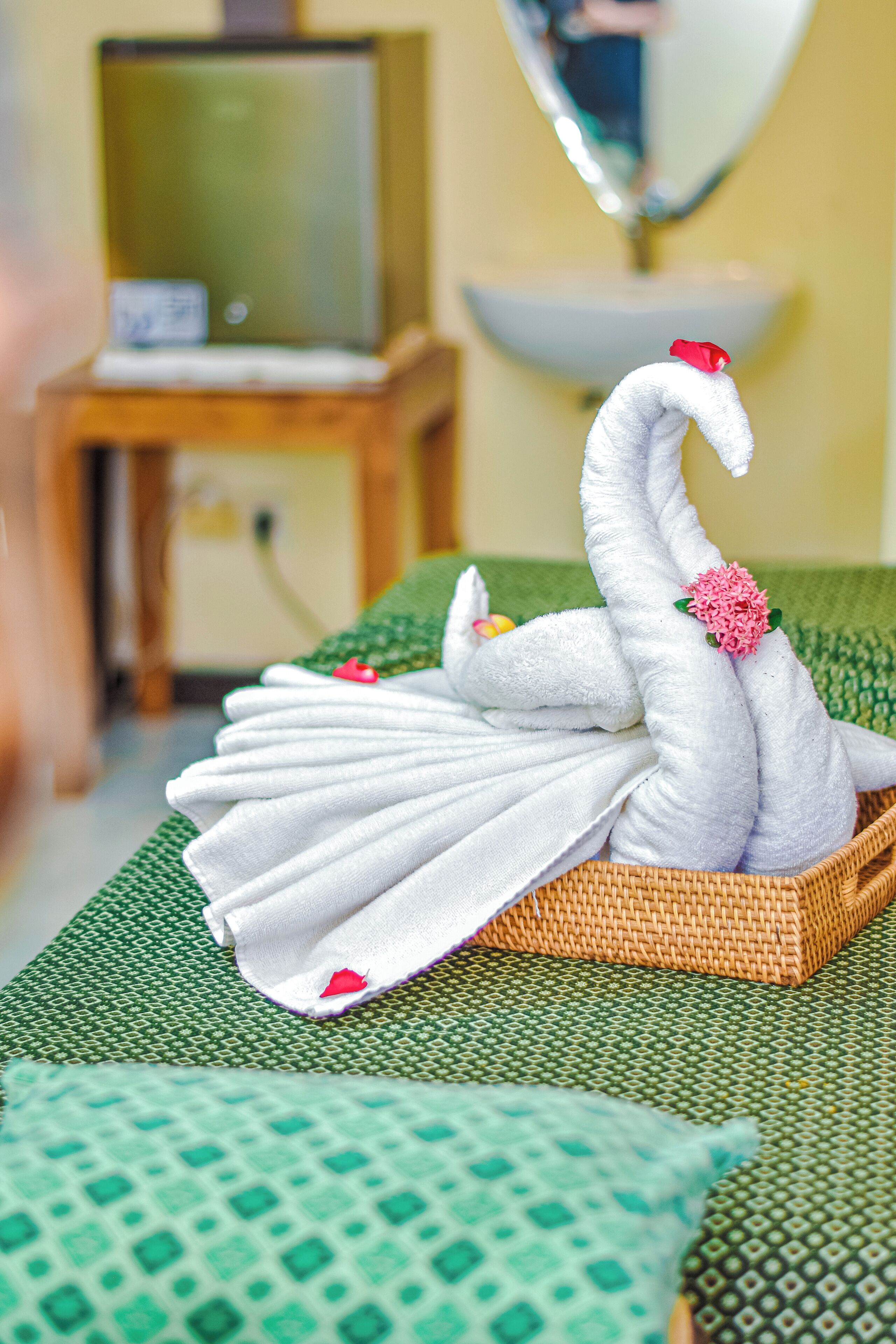 A swan-shaped towel arrangement on a bed with a green patterned bedspread.