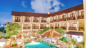 A hotel with a swimming pool, outdoor seating, and a thatched-roof structure.