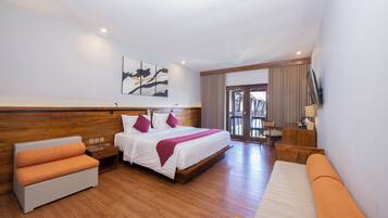 A hotel room with a large bed, a sofa, a wooden nightstand, a TV mounted on the wall, and a view of the outside balcony.