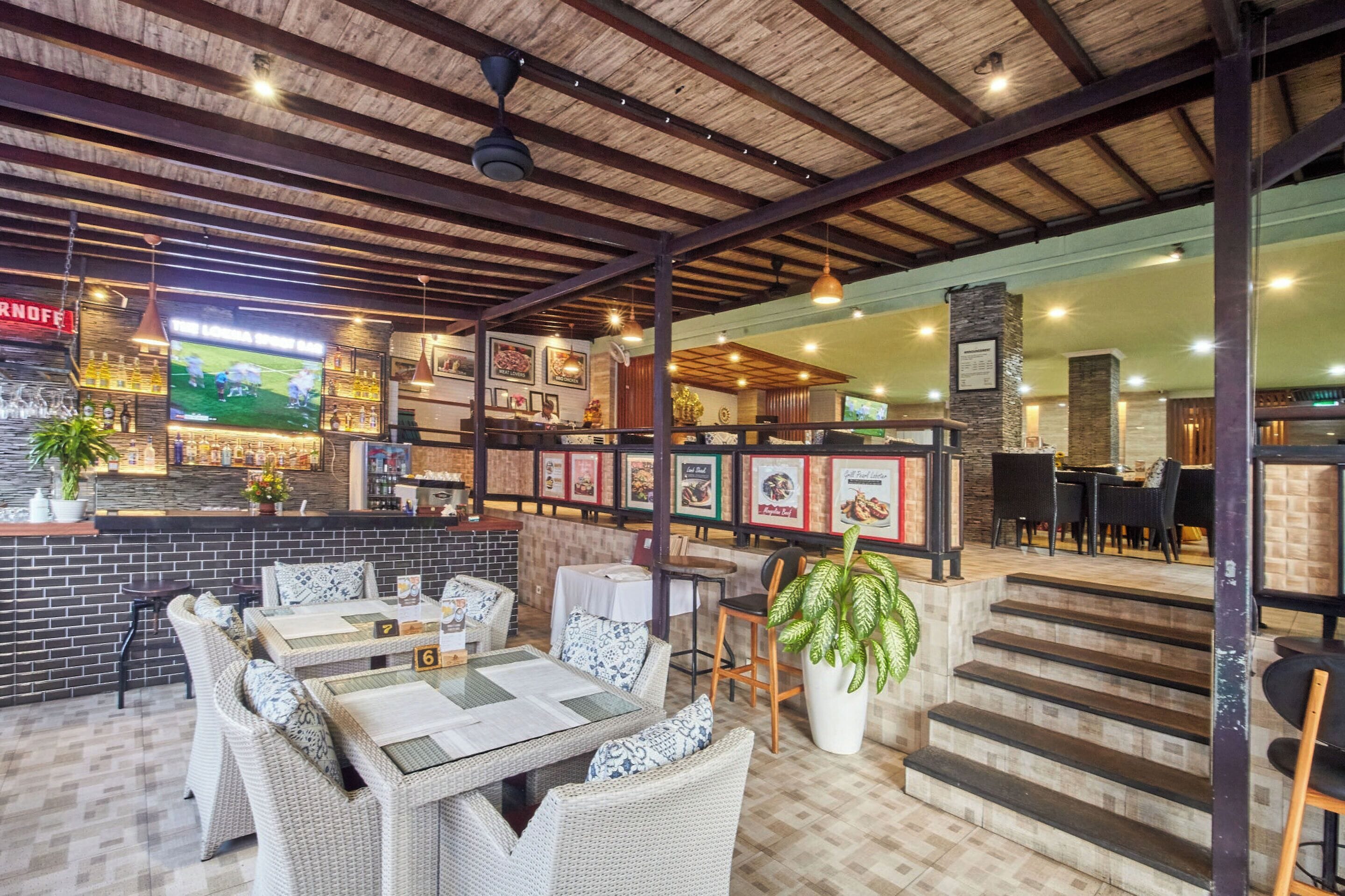 Een restaurant met rieten meubels, een bar en een trap naar een hoger gelegen verdieping.