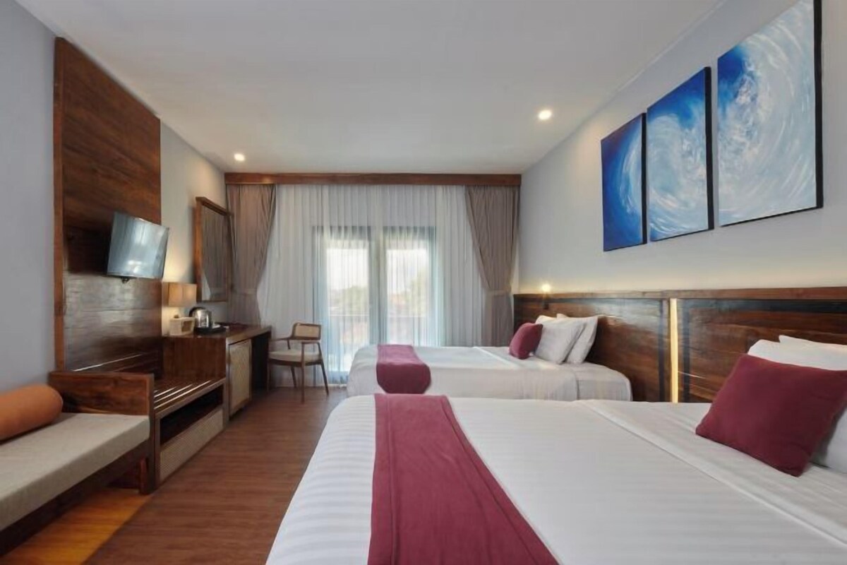 A hotel room with two beds, a TV, a desk, and a window with curtains.