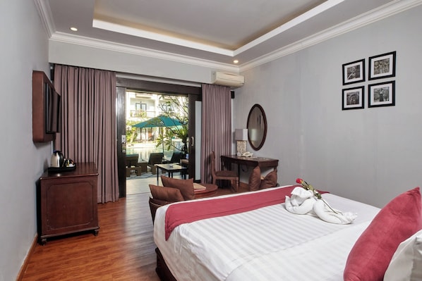 A hotel room with a bed, a desk, a chair, a TV, and a view of the outside.