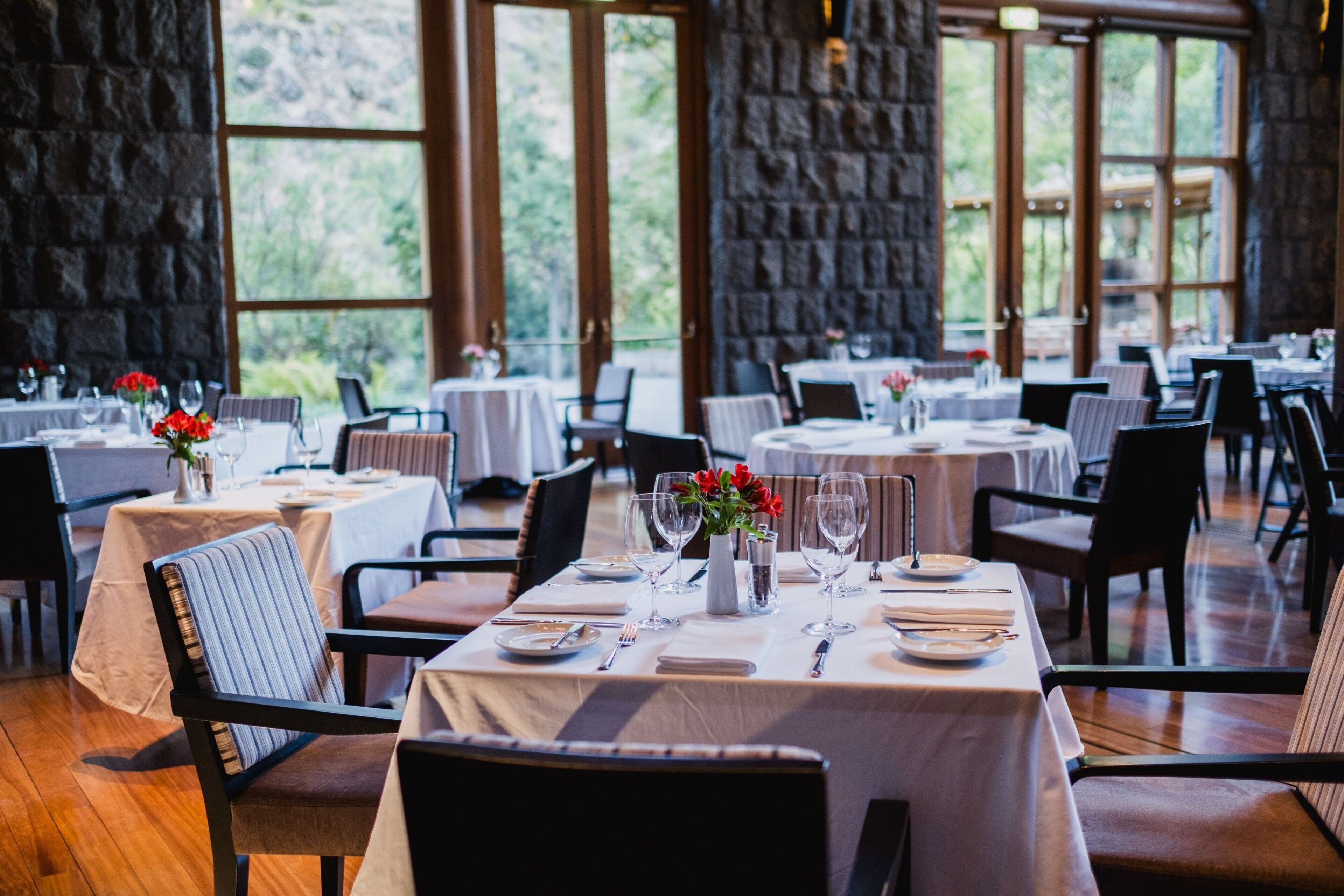 Un restaurante con mesas dispuestas para comer, que cuenta con una pared de piedra y amplios ventanales.