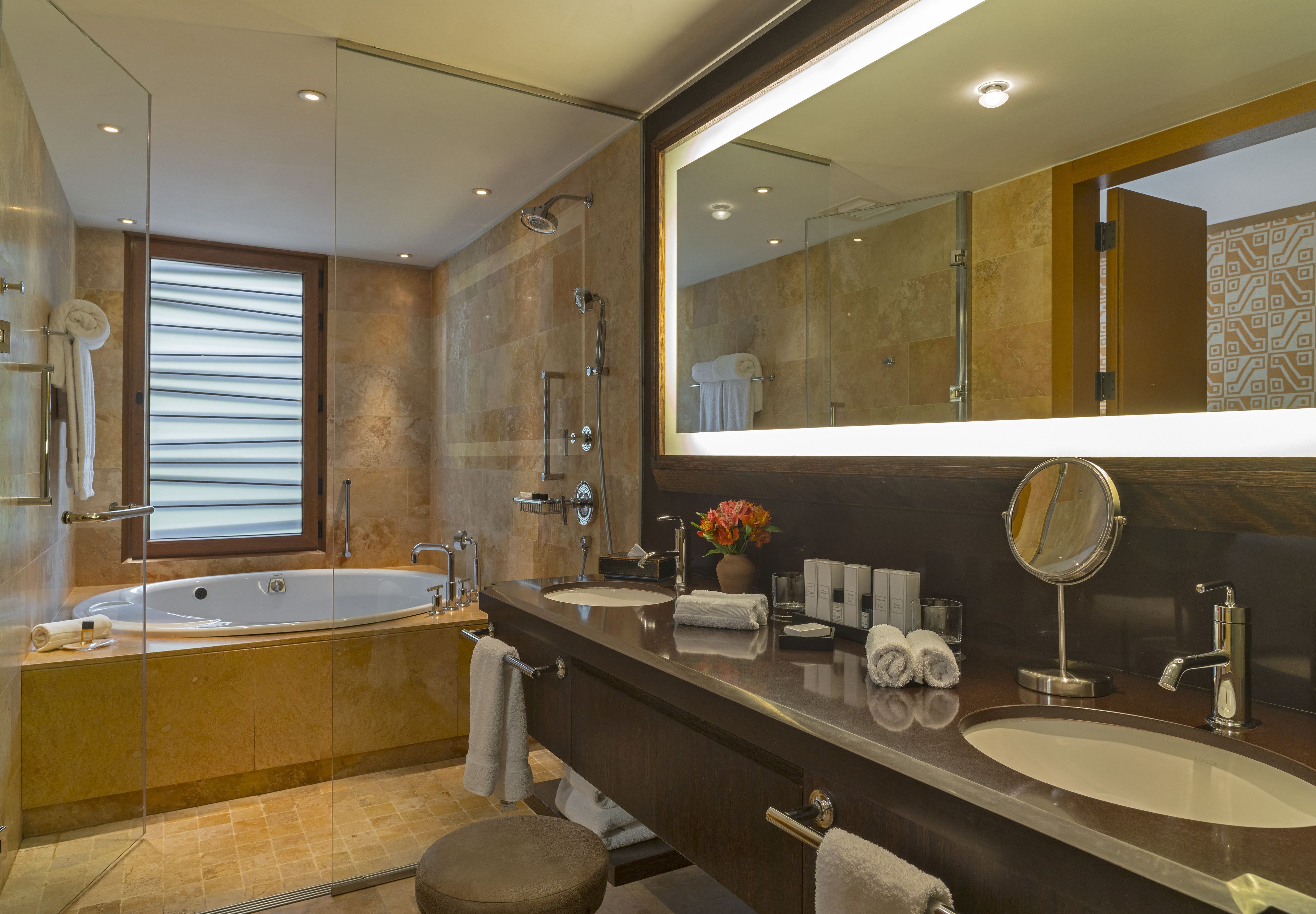 A modern bathroom with a large bathtub, two sinks, a vanity, and a large mirror.
