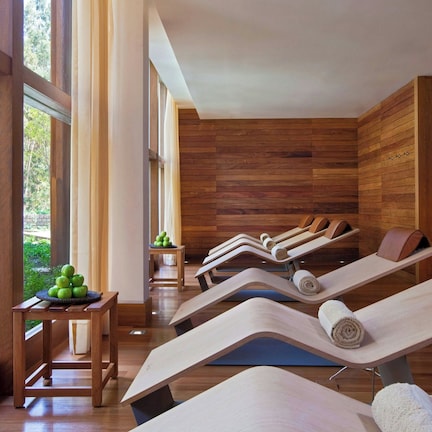 A spa room with wooden walls and large windows, multiple massage tables, and a small table with apples.