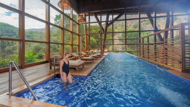 Une piscine intérieure avec vue sur un paysage montagneux, une terrasse en bois et un espace de détente.