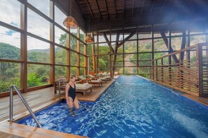 An indoor swimming pool with a view of a mountainous landscape, wooden deck, and lounge area. - Tambo del Inka, a Luxury Collection Resort & Spa (Urubamba)