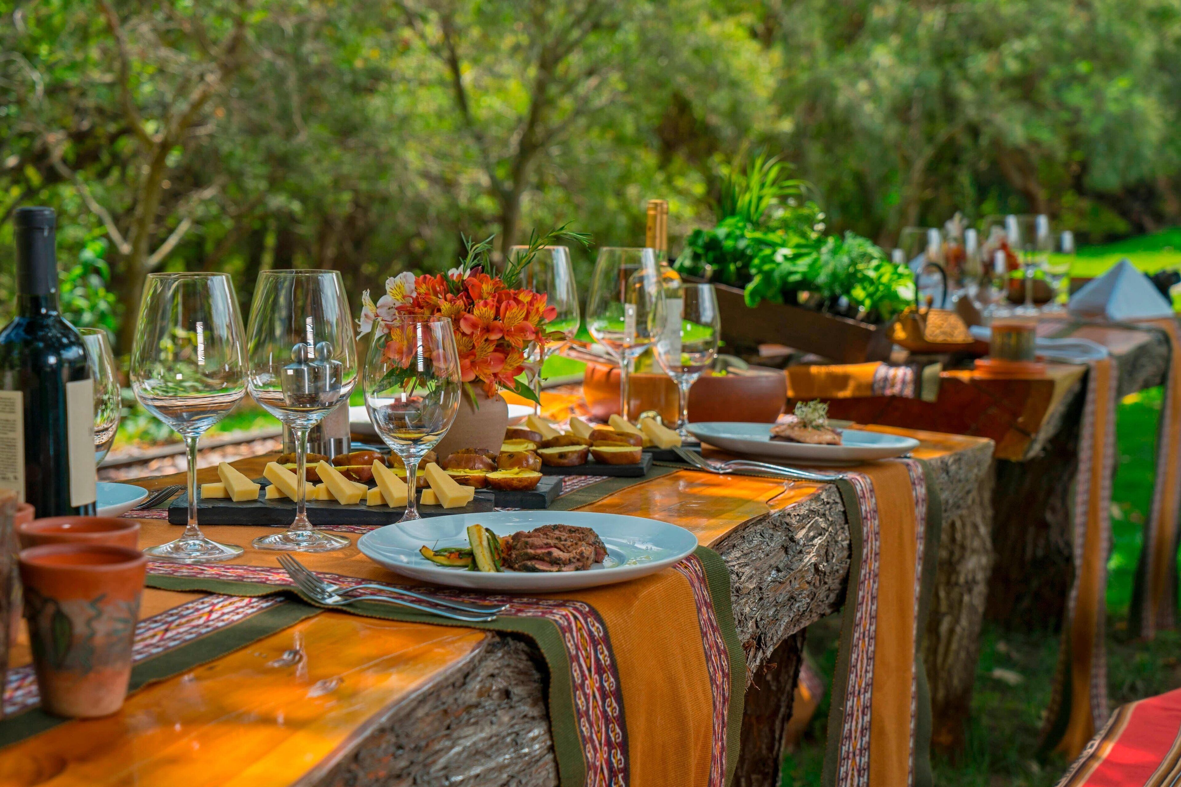 An outdoor dining table set with wine glasses, plates of food, and a bottle of wine.