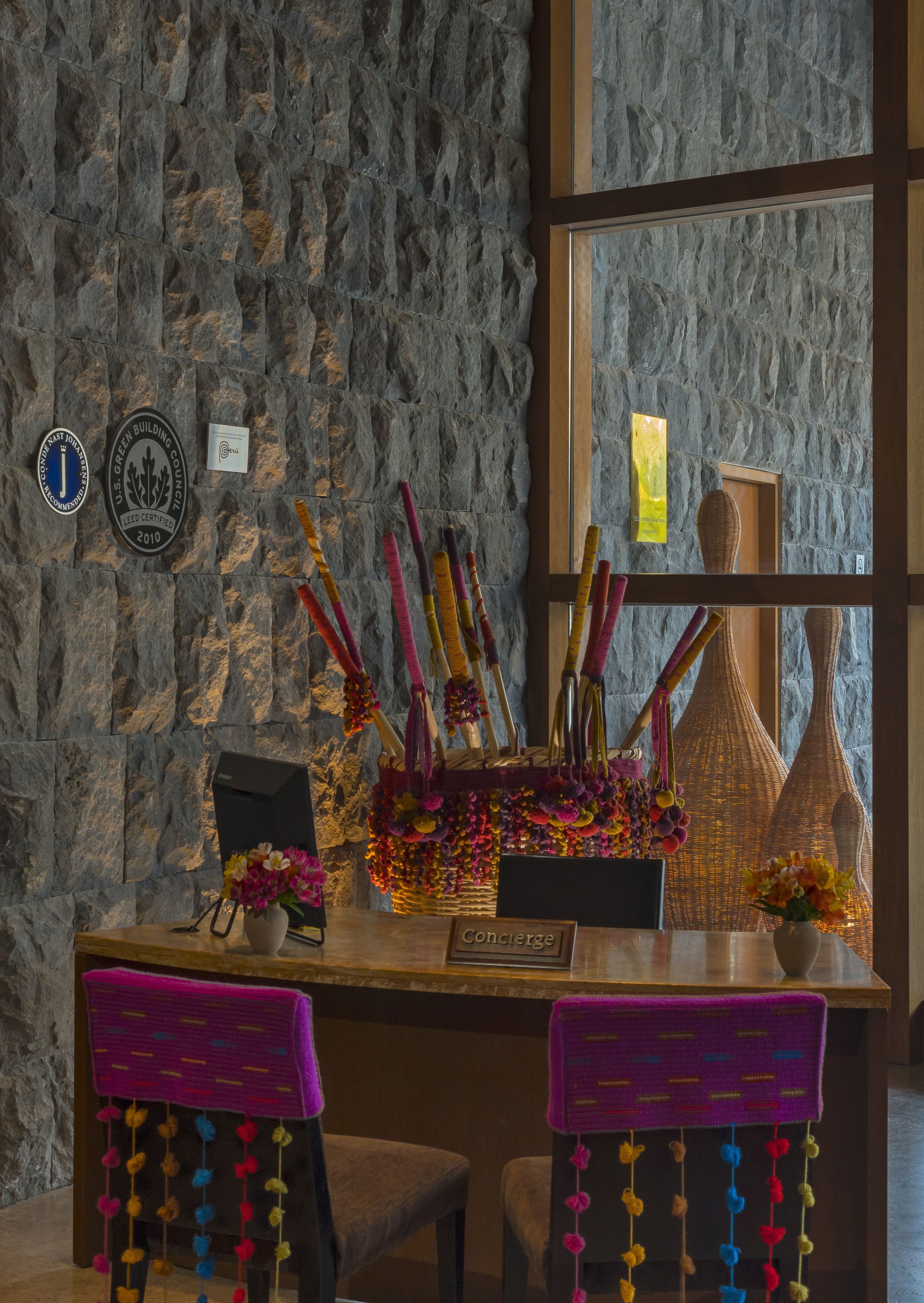 Un muro de piedra con placas de certificación LEED, un mostrador de recepción con un letrero que dice 'Concierge' y una ventana con cestas de mimbre.