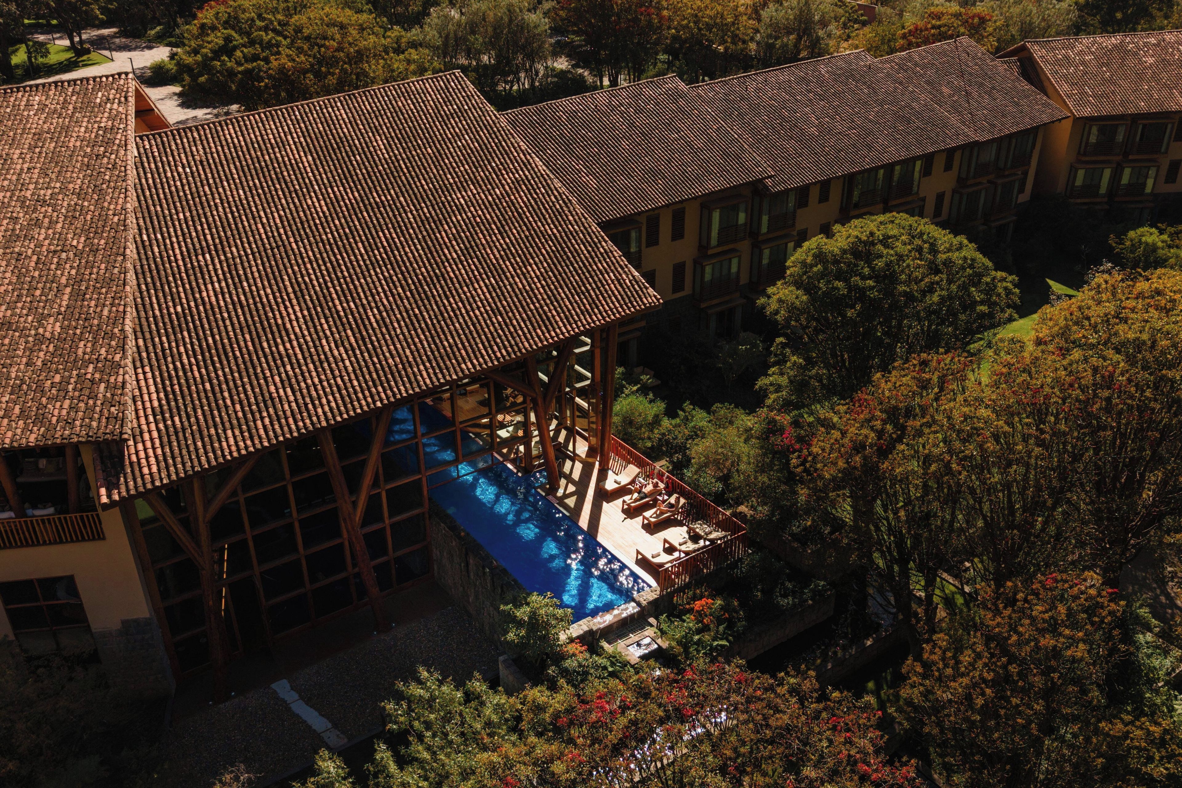 A building with a tiled roof, a swimming pool, and surrounding trees.