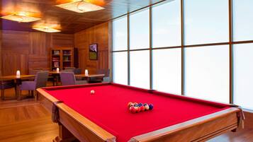 A pool table with a red felt surface, wooden walls, and large windows.