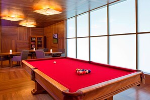 A pool table with a red felt surface, wooden walls, and large windows.
