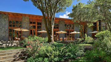 A building with stone walls and large windows, surrounded by a garden with steps leading up to outdoor seating areas.