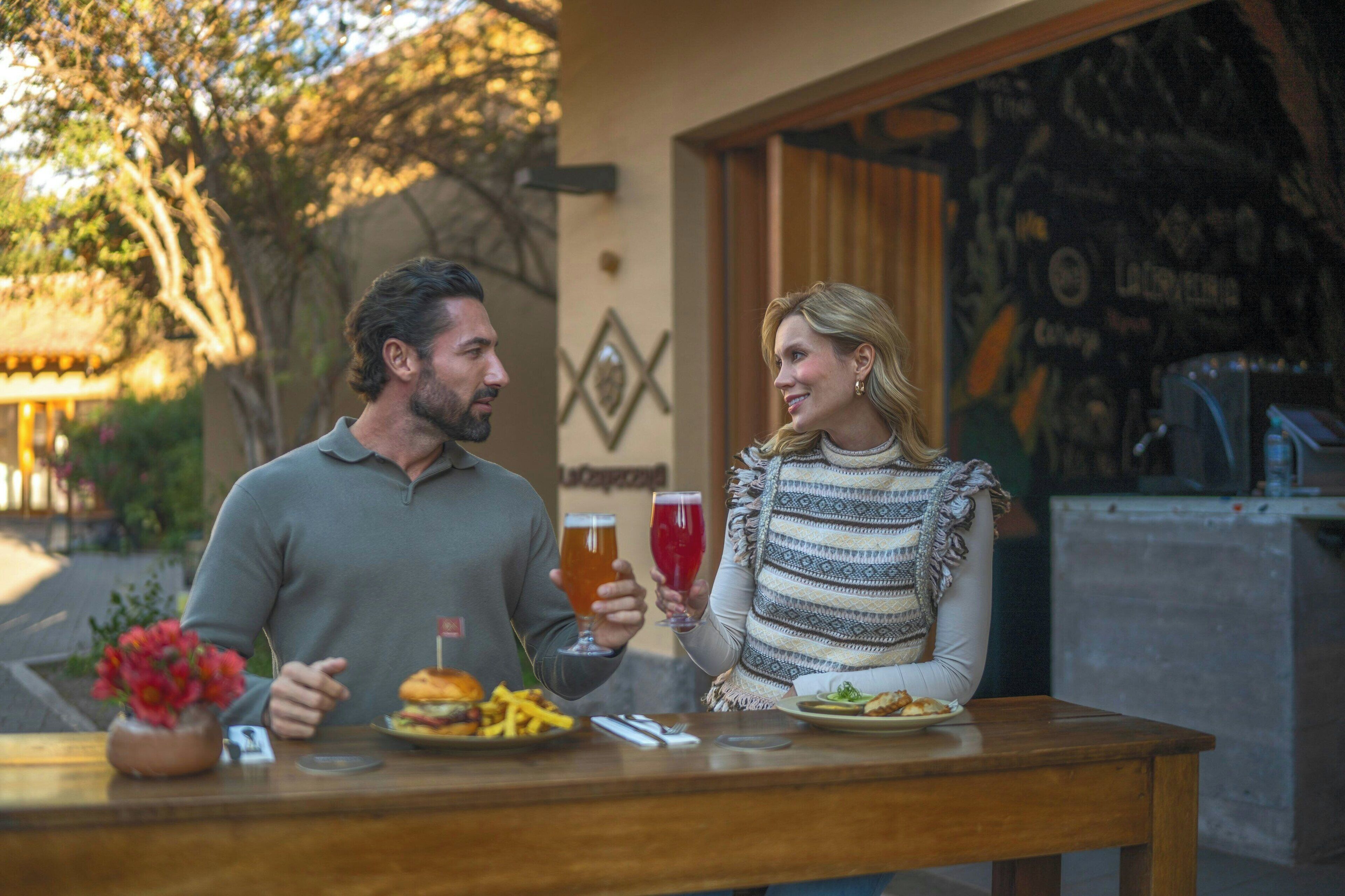 A couple dining at an outdoor restaurant with a table set for two, featuring a burger and fries.