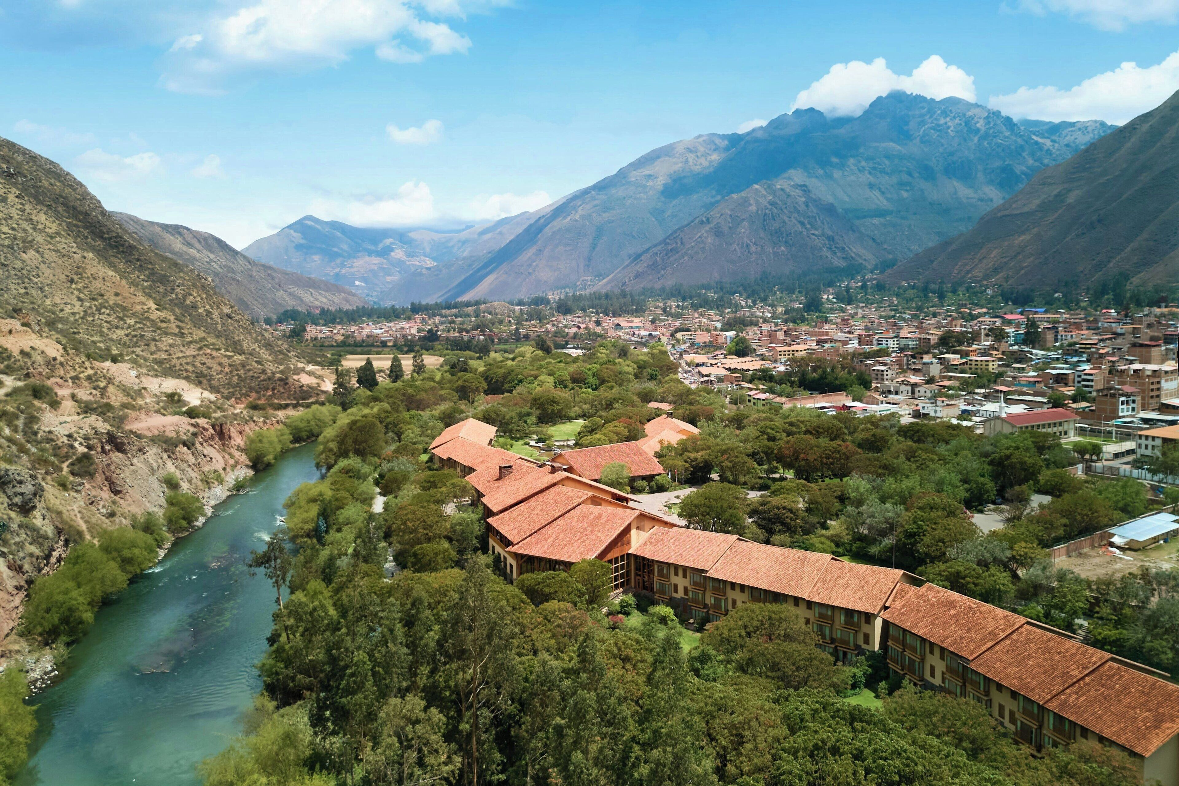 A mountainous landscape with a river, a town, and a building with a red roof.