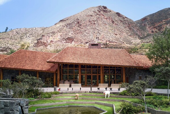 A stone building with a tiled roof, large windows, and a landscaped garden with a pond.
