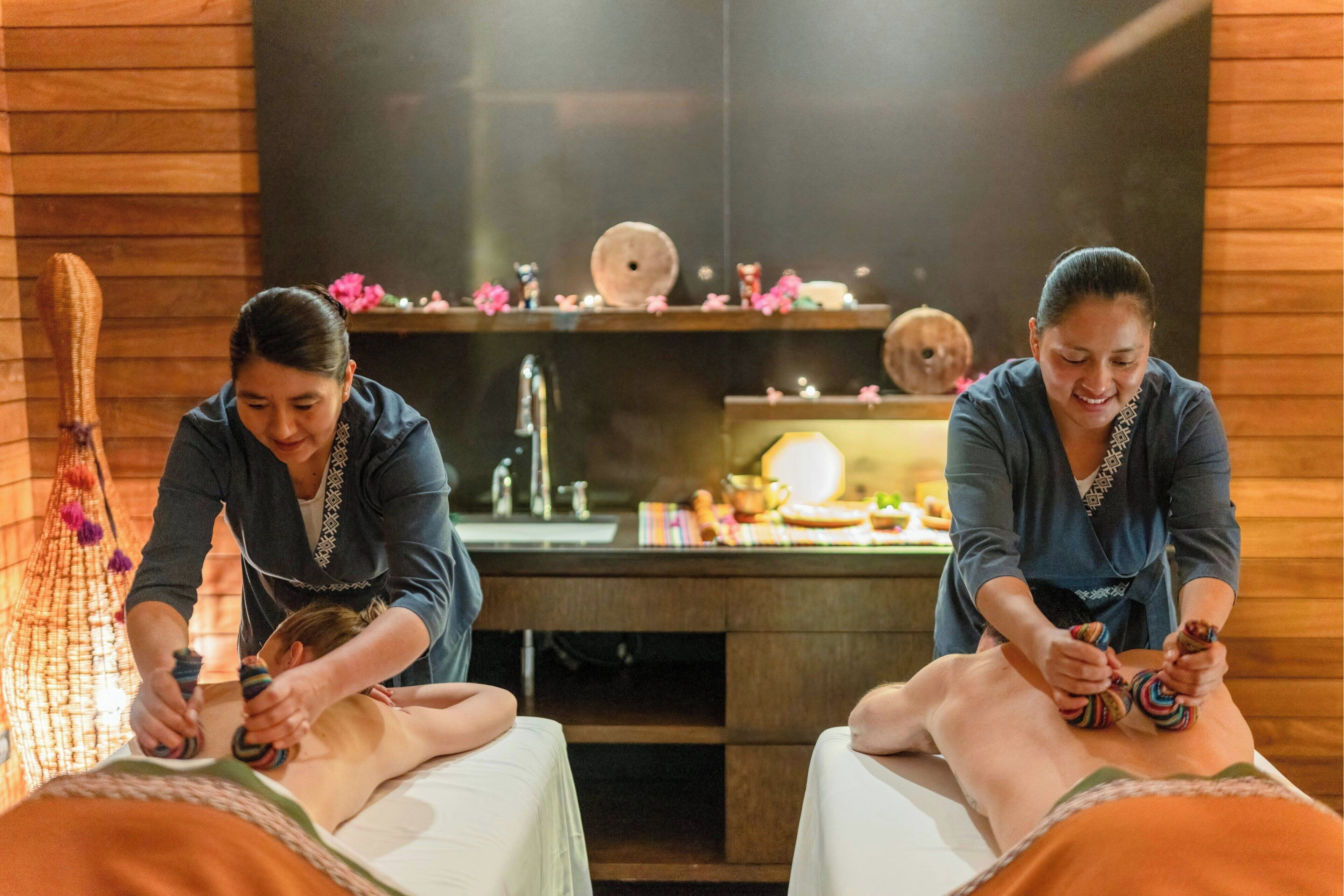 A massage therapy room with wooden walls, a massage table, and a small shelf with decorative items.