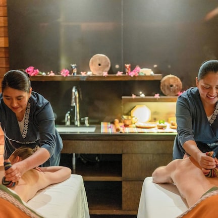 A massage therapy room with wooden walls, a massage table, and a small shelf with decorative items.