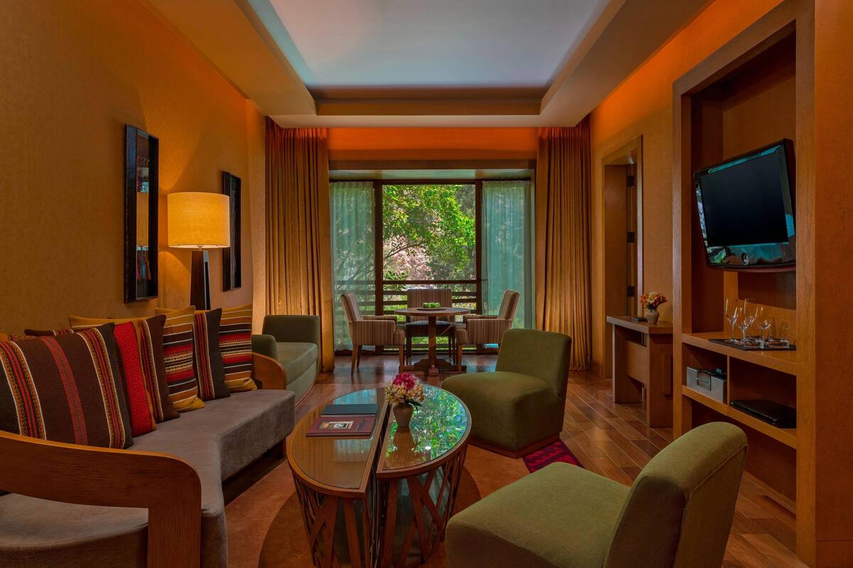A hotel room with a sofa, chairs, a dining table, a TV, and a window with curtains.