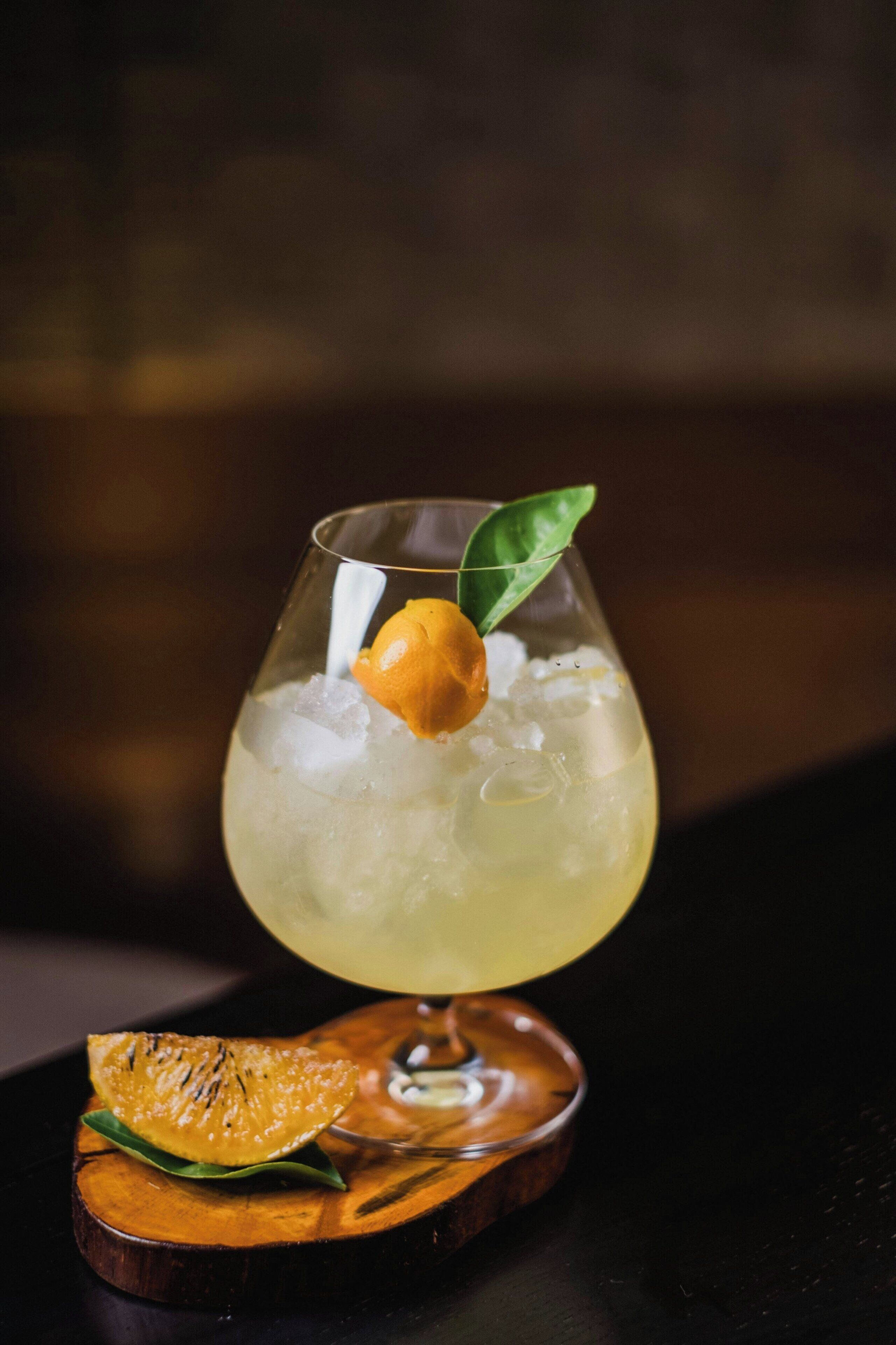 A cocktail glass with ice and a garnish on a wooden coaster.