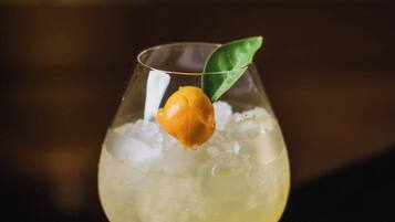 A cocktail glass with ice and a garnish on a wooden coaster.