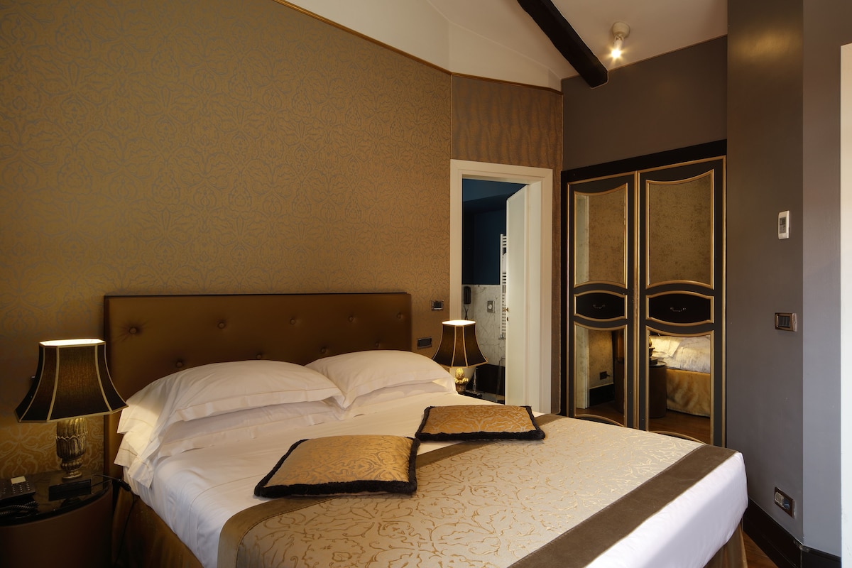 A hotel room with a large bed, two bedside lamps, a nightstand, and a mirror with a door.
