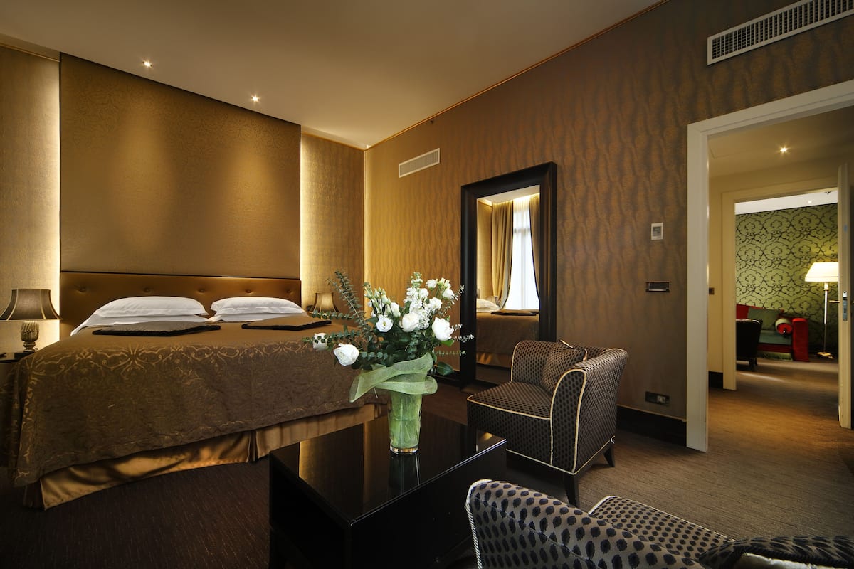 A hotel room with a bed, a chair, a table, and a vase with flowers.