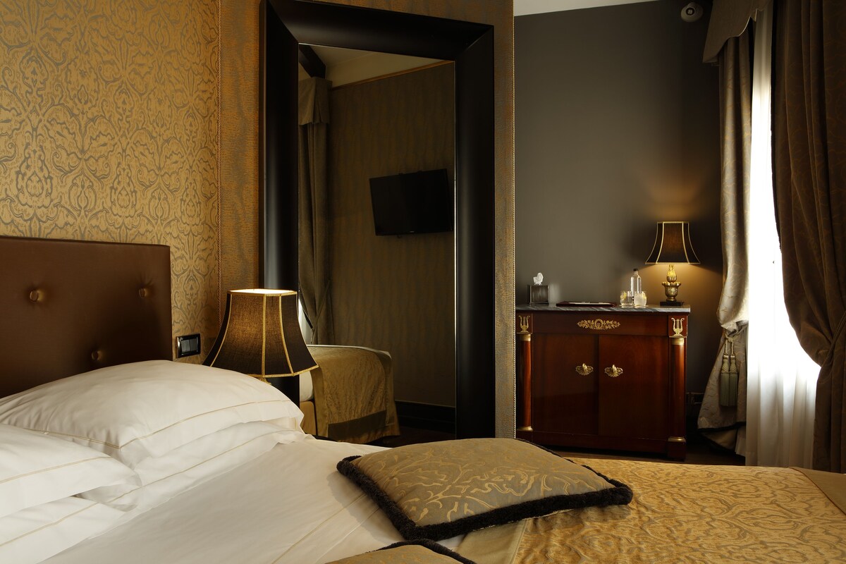 A hotel room with a bed, a desk, a lamp, and a television on the wall.