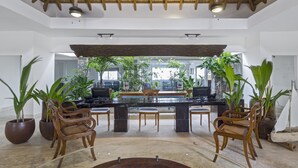 Amplio espacio interior con una mesa central, sillas de mimbre y grandes plantas en macetas.