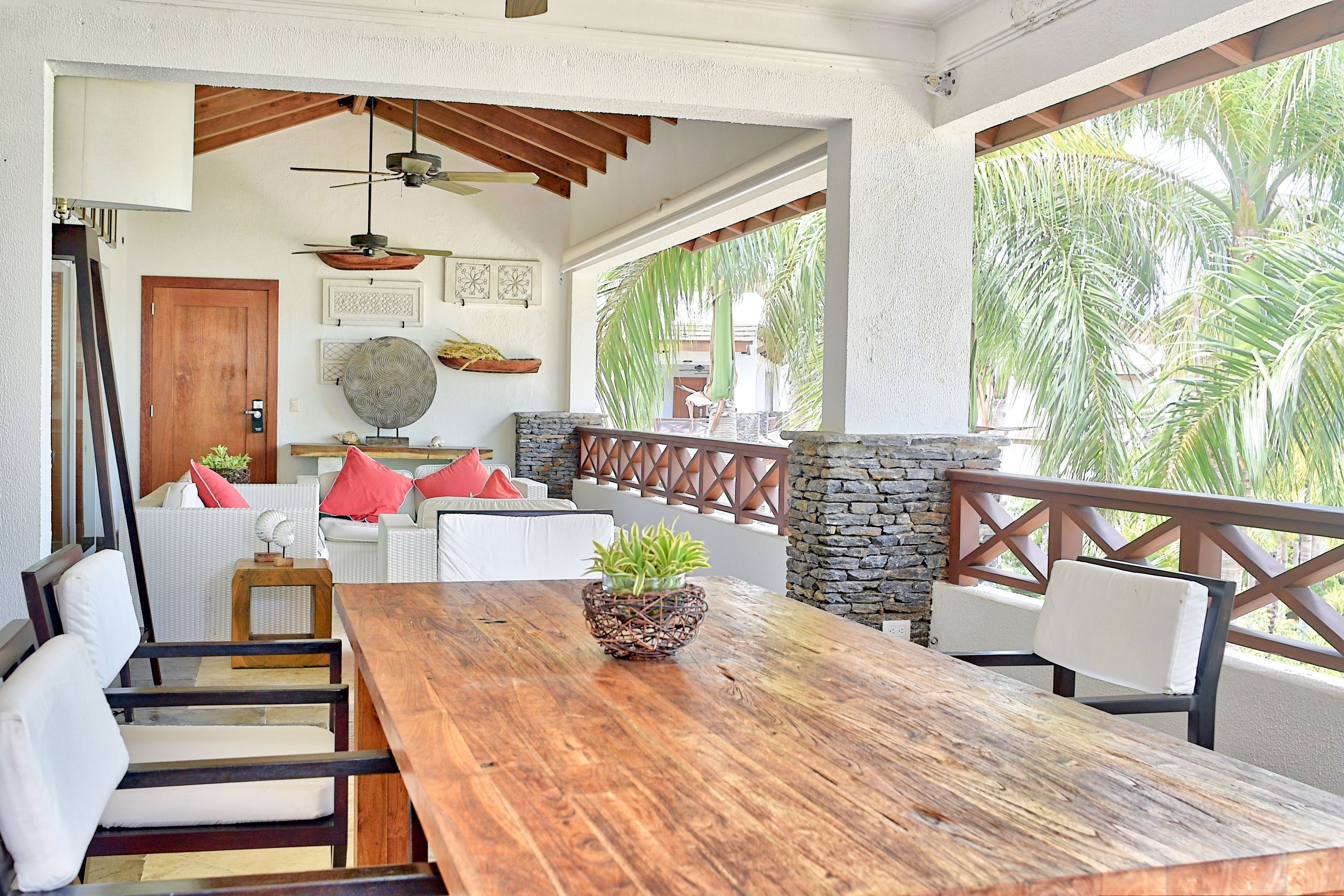 A wooden dining table with chairs, a potted plant, and a stone wall with a wooden railing.