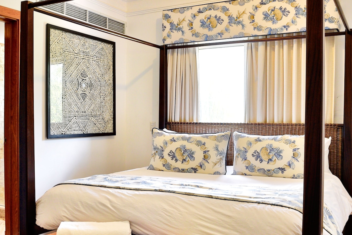 A four-poster bed with a canopy, a framed abstract artwork on the wall, and a window with curtains.