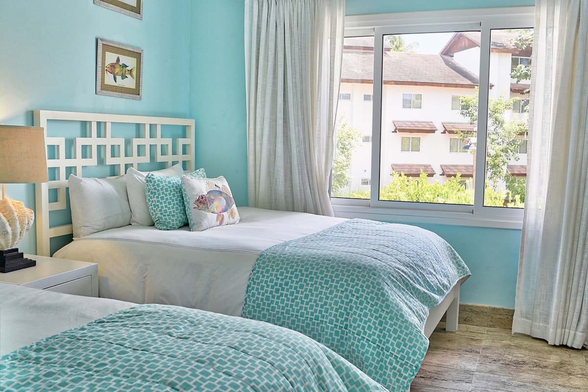 A bedroom with a bed, a nightstand, a lamp, and a window with curtains.