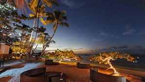 Un espacio de descanso frente al mar con mobiliario de mimbre e iluminación con luces colgantes.