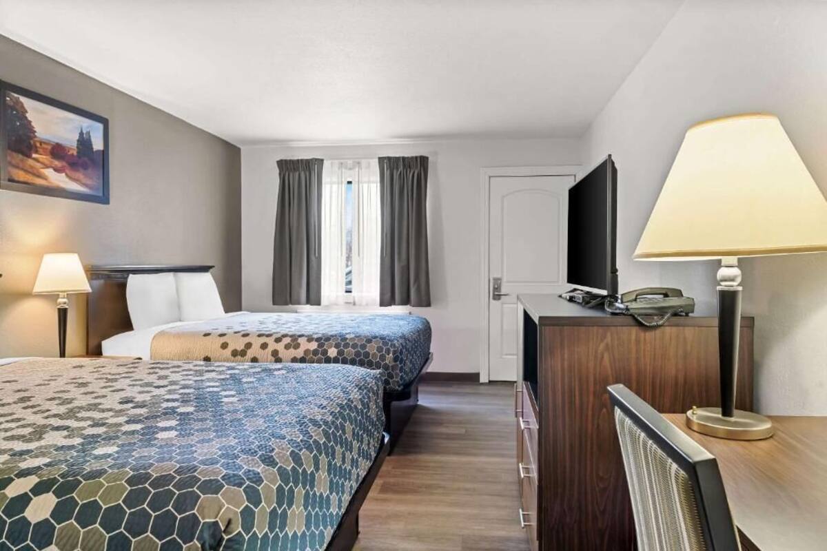 A hotel room with two beds, a desk, a chair, a TV, and a lamp.