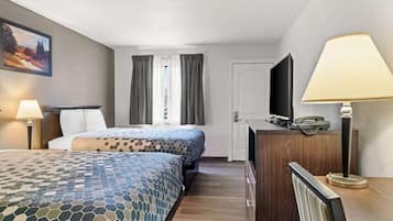 Une chambre d’hôtel avec deux lits, un bureau, une chaise, une télévision et une lampe.