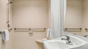 A bathroom with beige tiles, a white sink, a mirror, and a shower with a handheld showerhead.