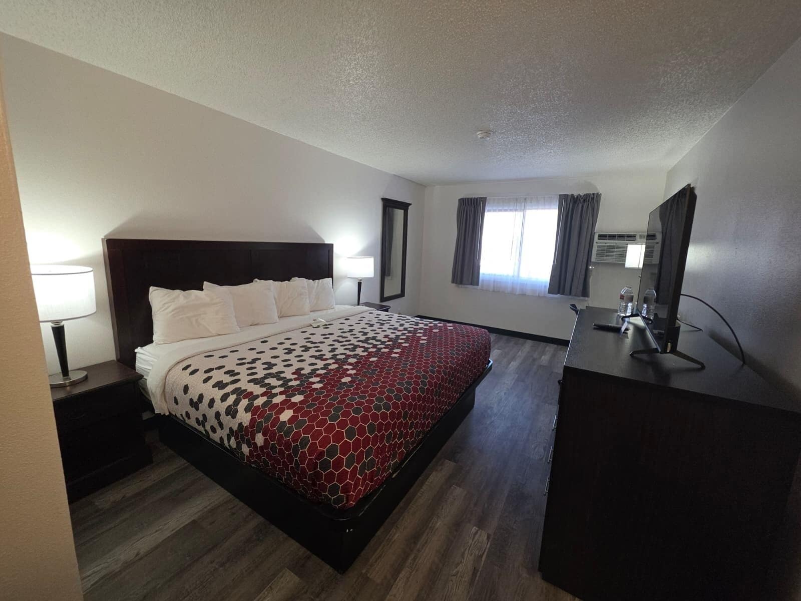 A hotel room with a large bed, a desk, a chair, a TV, and a window with curtains.