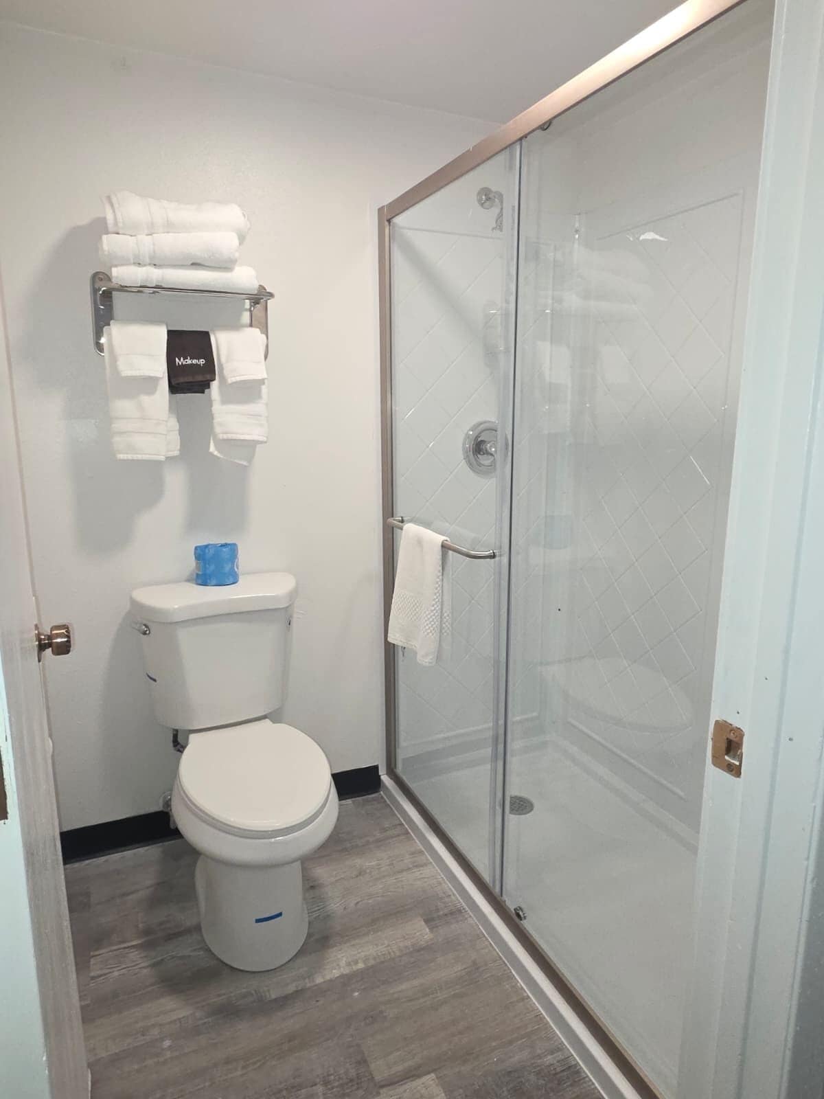 Un baño con inodoro, ducha con cortina de vidrio y toallero con toallas dobladas.