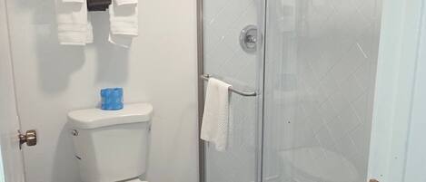 Un baño con inodoro, ducha con cortina de vidrio y toallero con toallas dobladas.