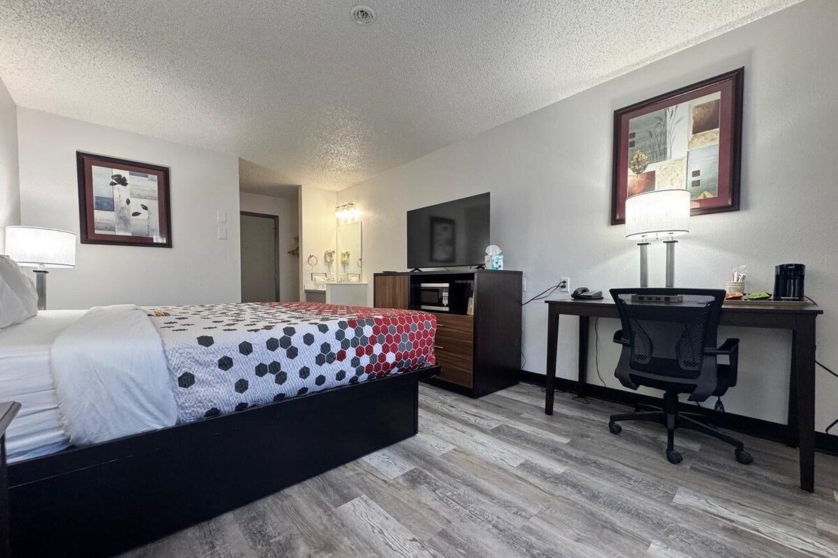 A bedroom with a bed, a desk, a chair, a TV, and a microwave.