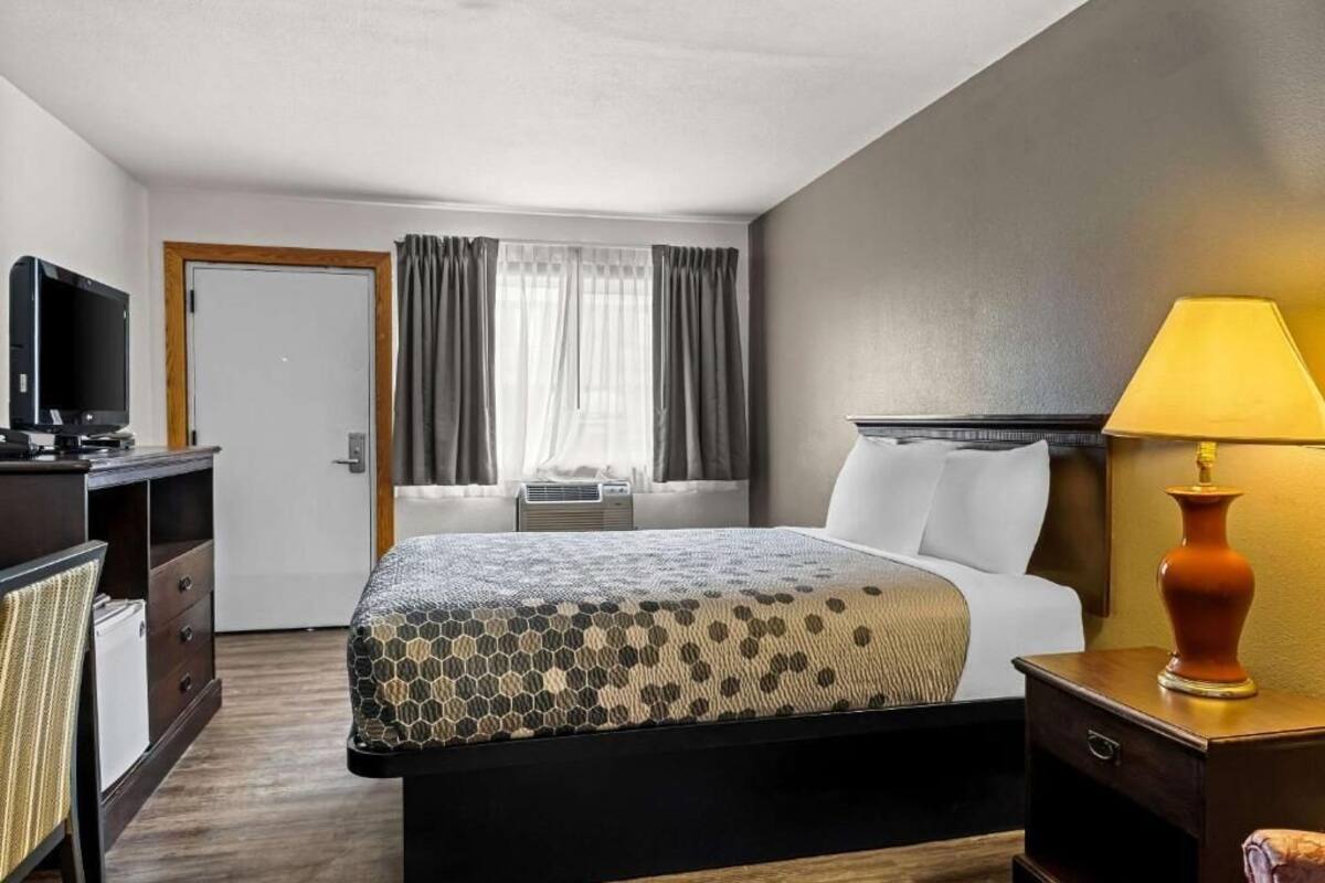 A hotel room with a bed, a television, a desk with a lamp, and a window with curtains.