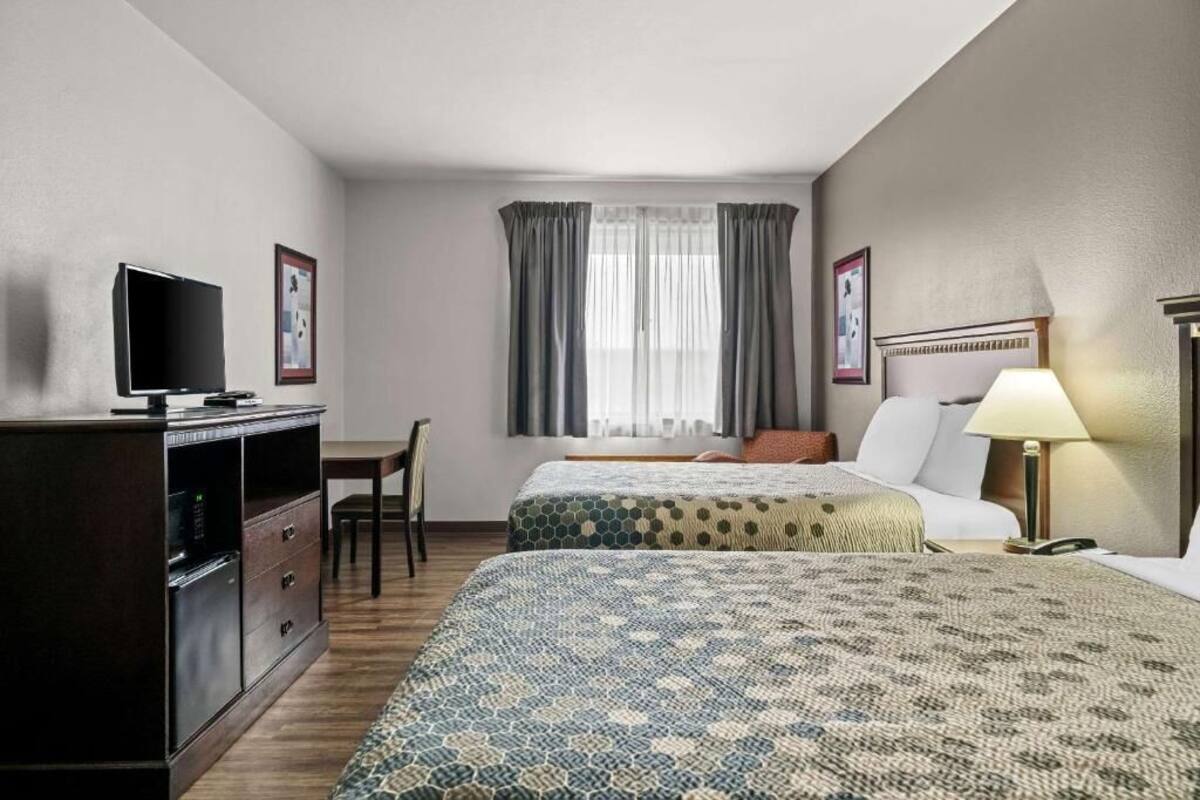 A hotel room with two beds, a desk, a TV, and a window with curtains.