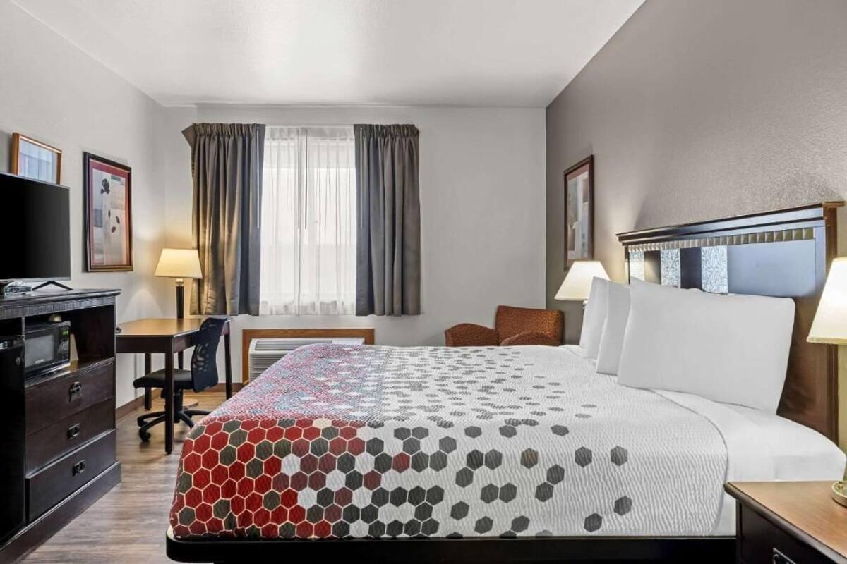 A hotel room with a large bed, a desk, a chair, a TV, and a window with curtains.