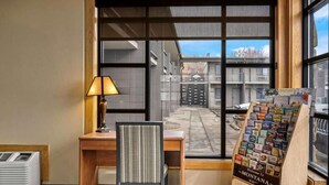 Une chambre d’hôtel équipée d’un bureau, d’une chaise, d’une lampe, d’un climatiseur et d’une fenêtre donnant sur des immeubles.