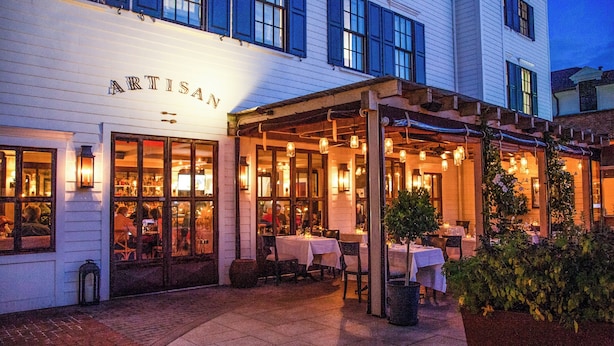 A restaurant with outdoor seating, a white facade, and a sign reading "ARTISAN". - Delamar Southport (Southport)