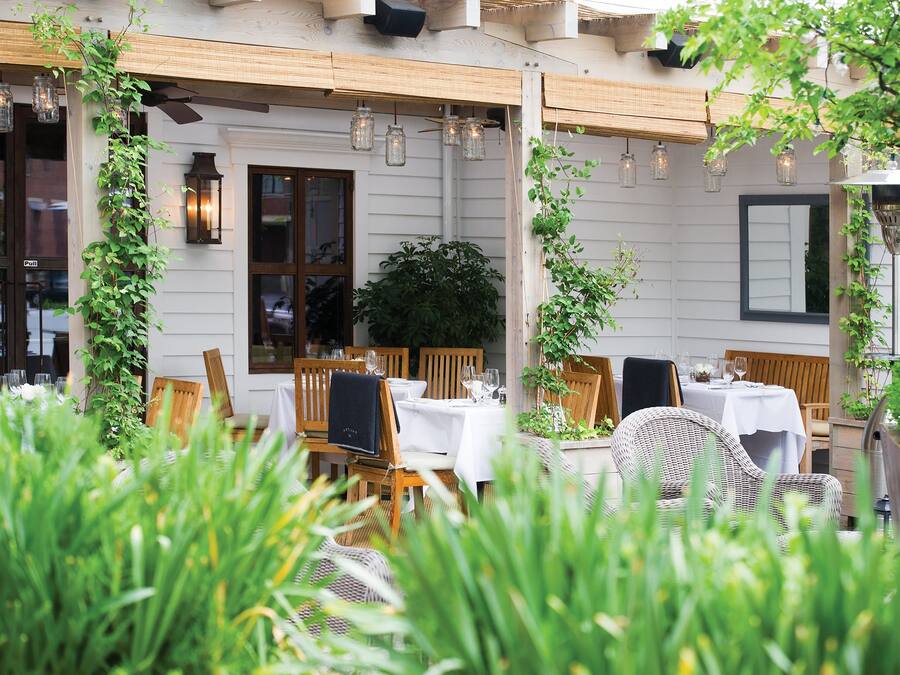 An outdoor dining area with tables and chairs, surrounded by greenery and string lights.