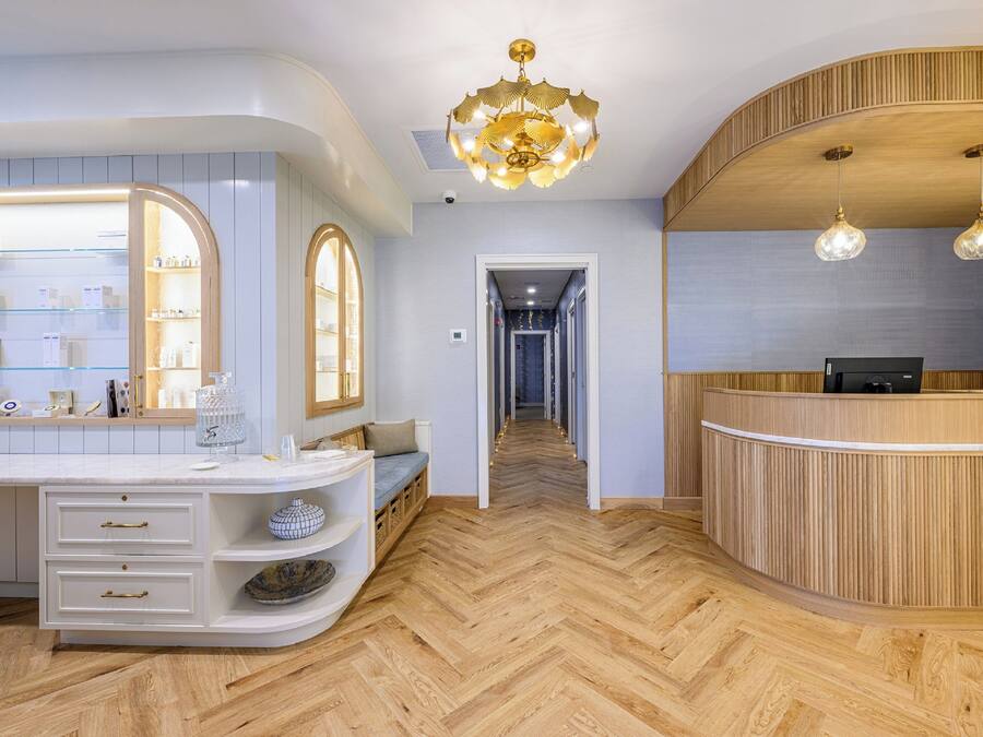 A modern hotel lobby with a wooden reception desk, a large mirror, and a herringbone floor pattern.