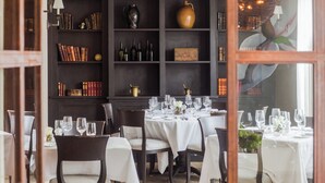 A dining area with round tables set for a meal, surrounded by dark wooden bookshelves filled with books and decorative items. - Delamar Southport (Southport)