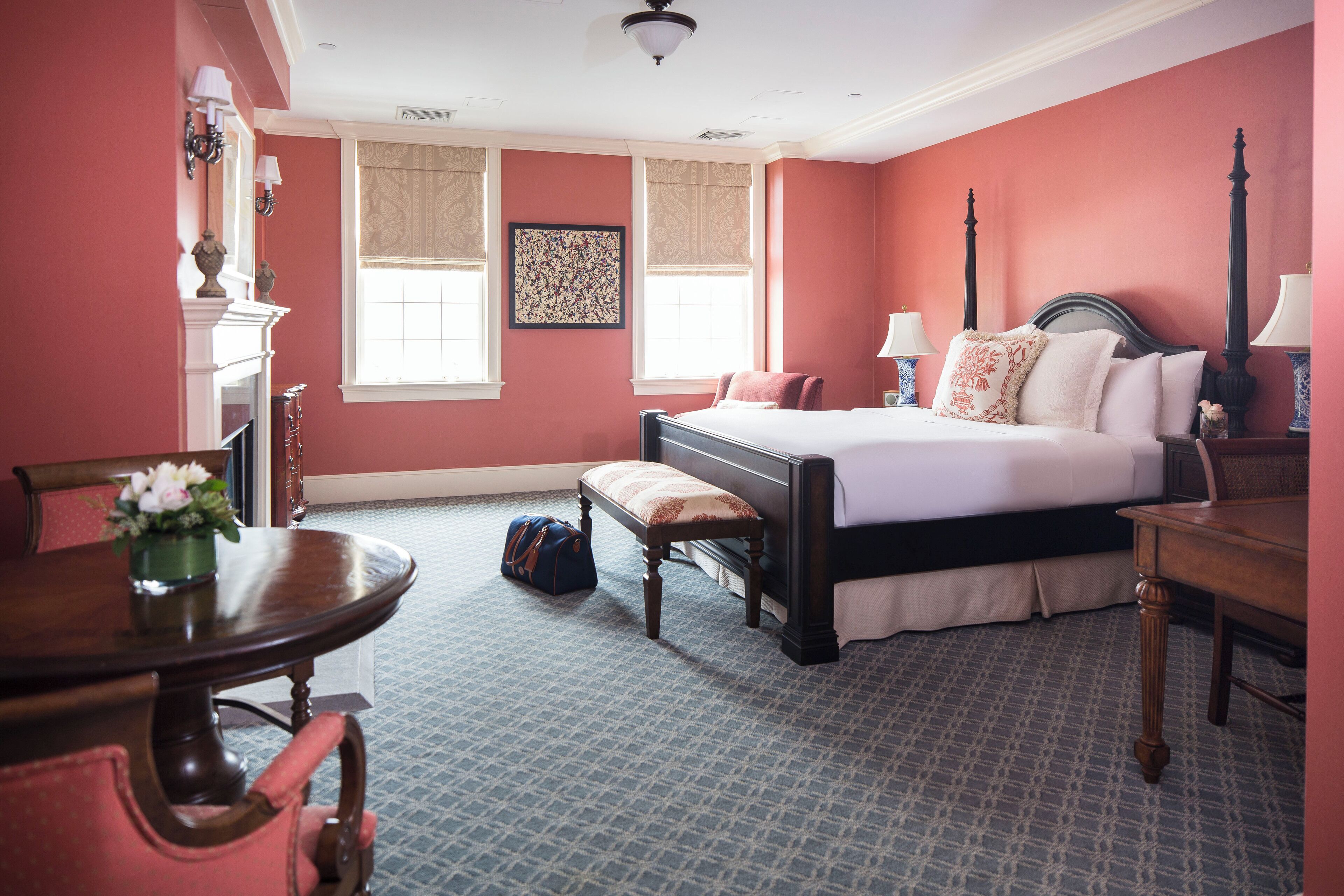 Une chambre d’hôtel avec un grand lit, un bureau, une chaise, une petite table et une cheminée.